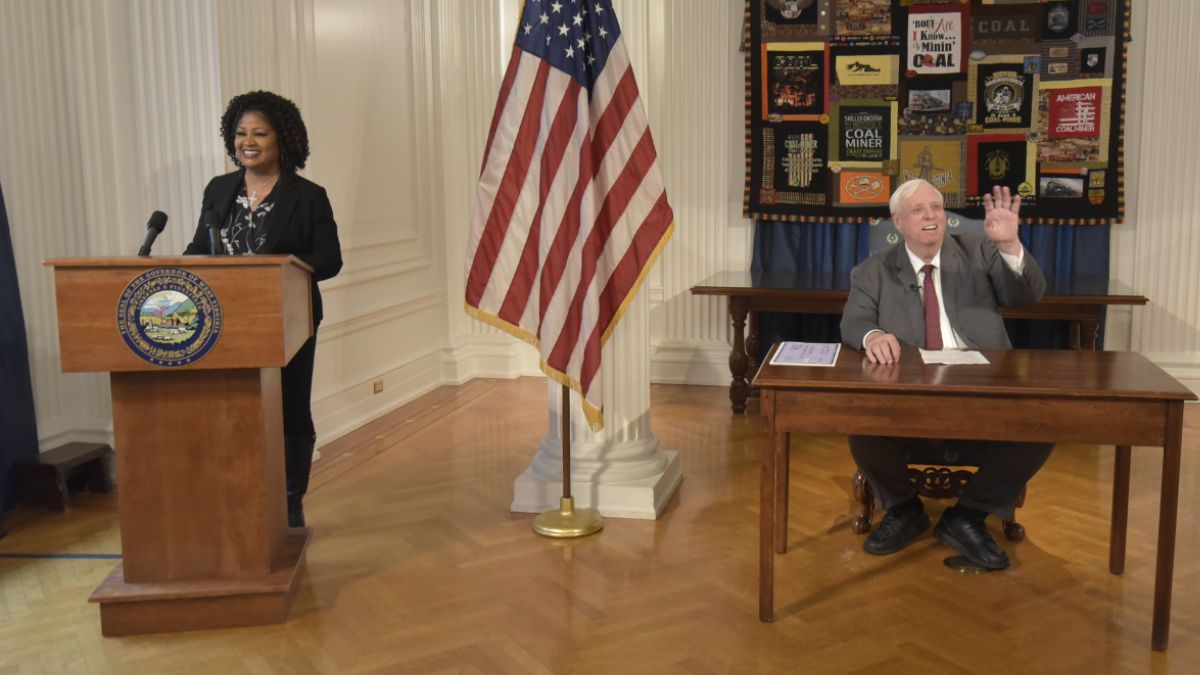 Executive Director Jill Upson at Podium and Governor Jim Justice at Desk Awarding BRIDGE Grants in Kanawha County