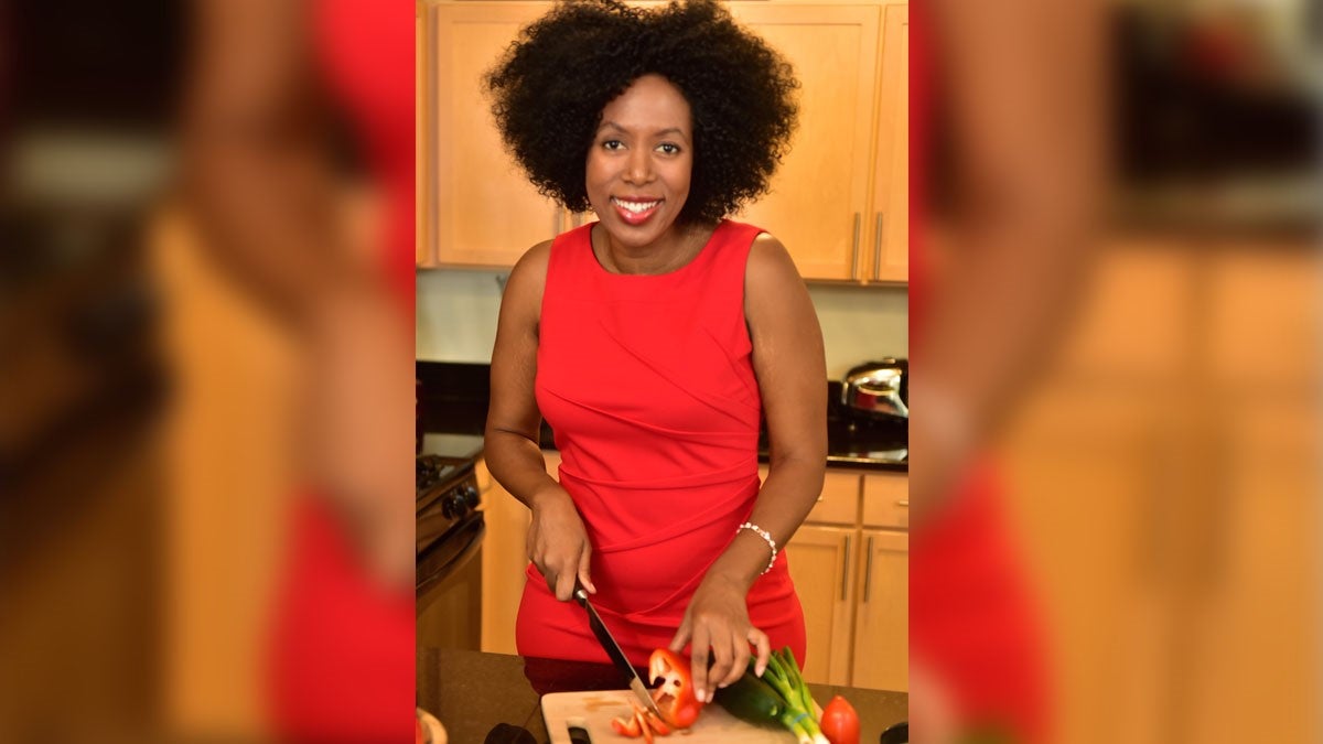 Ruby Lathon in Red Dress Cutting Vegetables in Wood Cabinet Kitchen
